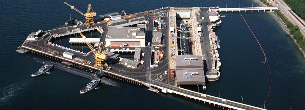 Delta Pier at Naval Base Kitsap-Bangor, Washington, as viewed from the air above Hood Canal.  The unique design of the Delta Pier was constructed parallel to the shoreline for ecological preservation reasons, and has one of the largest dry docks built by the Navy. It can support simultaneous maintenance on five of Pacific Fleet’s eight assigned Trident submarines at one time.